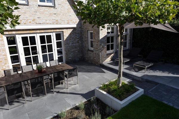 Ruim keramisch terras met eettafel en loungehoek in een verzorgde tuin
