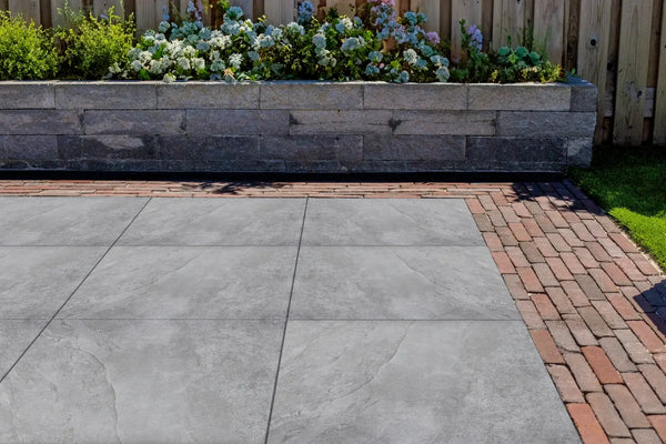 Keramisch terras met natuursteenlook naast een stapelmuur van natuursteen en een klinkerpad